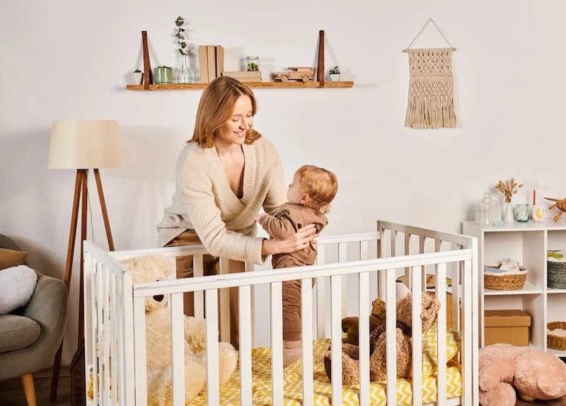 Mother putting toddler into crib