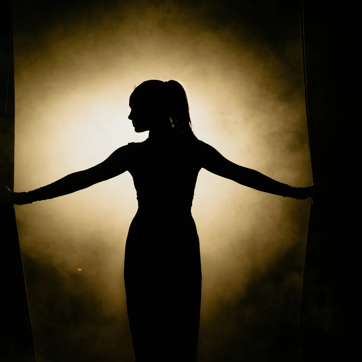 Silhouette of a model stepping through stage curtains into the spotlight at a fashion show